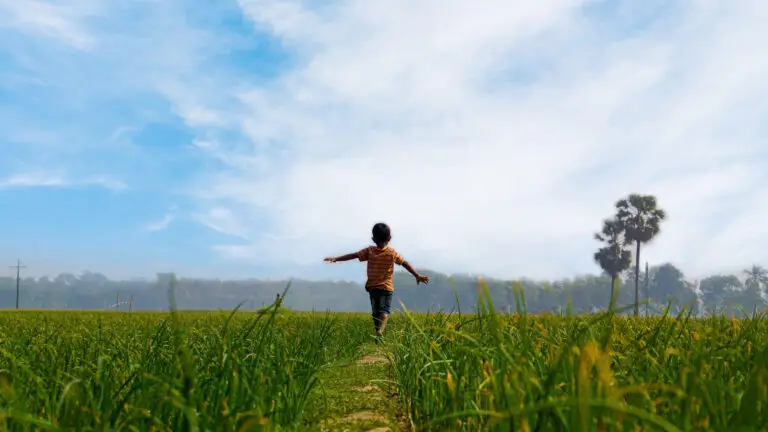 Child with arms outstretched running through a green field under a blue sky