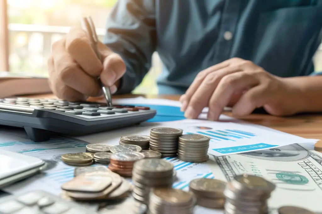 Person using a calculator with stacks of coins and money on a desk