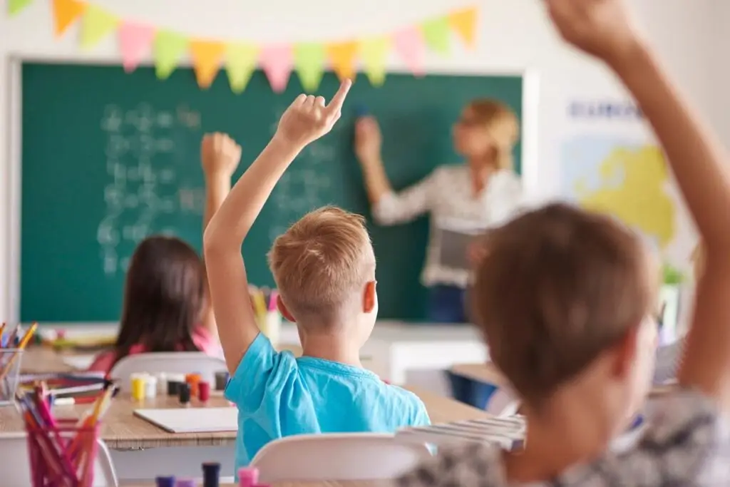 Image of children in a classroom raising their hands