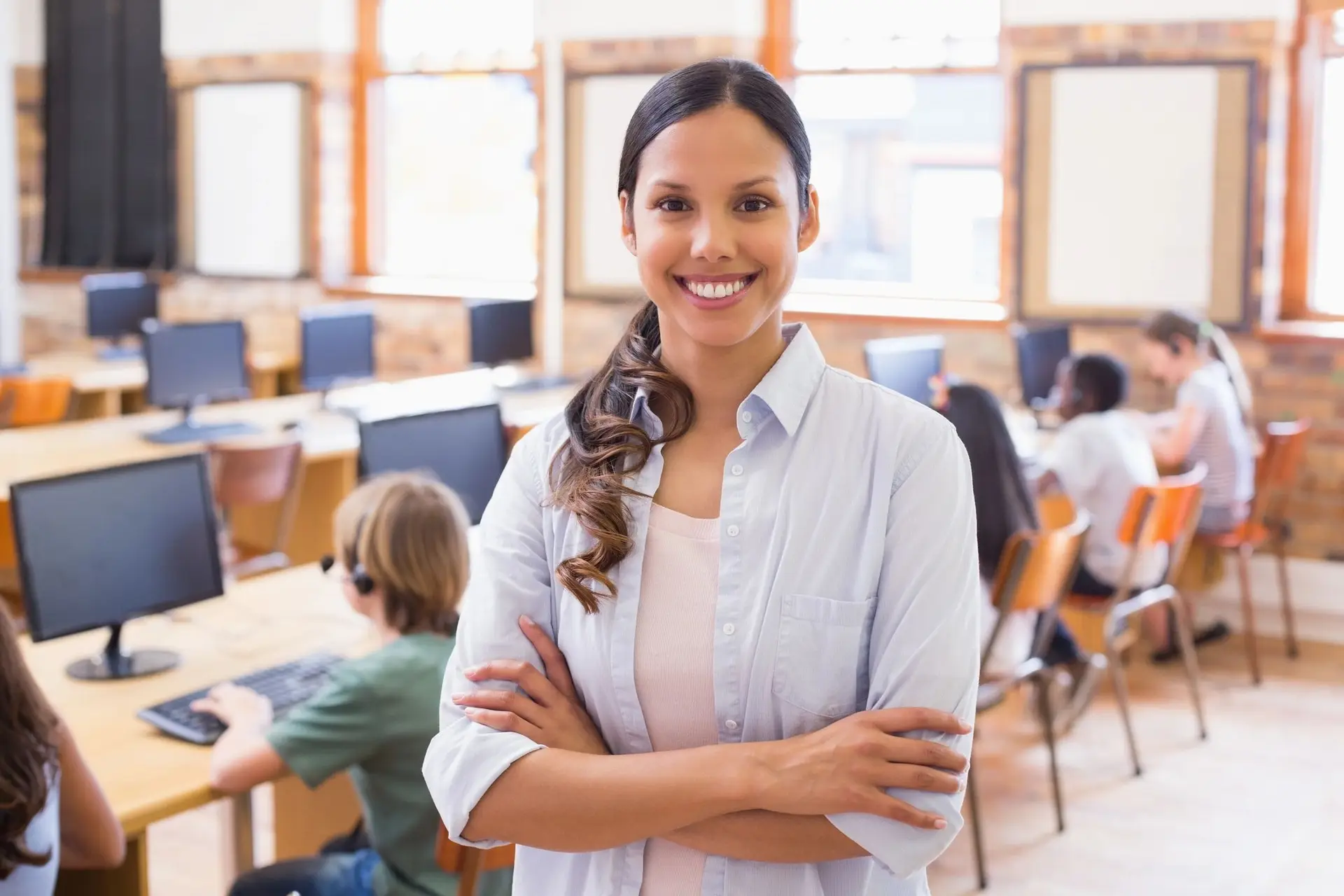 Teacher standing in computer lab with arms crossed smiling