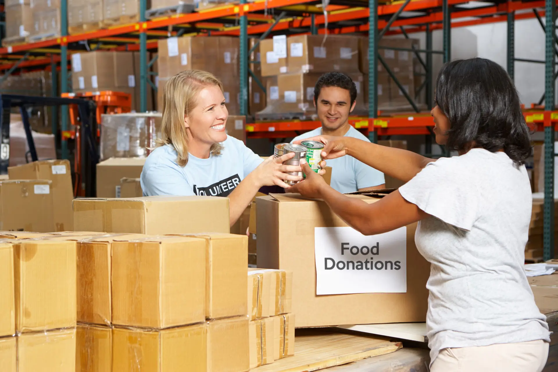 Volunteers sorting canned food donations in a warehouse filled with boxes